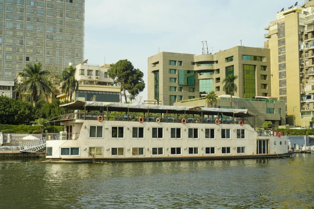 A serene scene of a cruise boat on the Nile River in Cairo, Egypt, with modern buildings in the background.