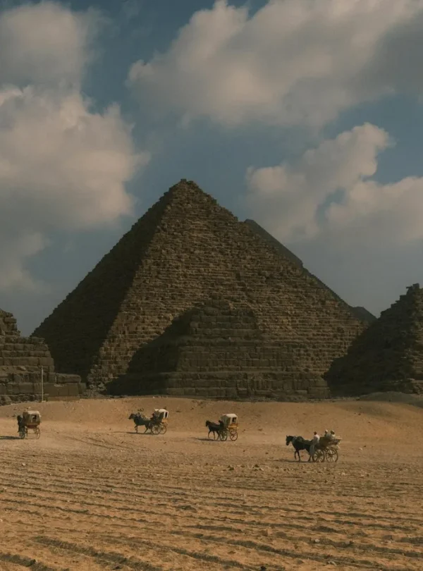 Majestic shot of the Pyramids of Giza with camels in the foreground under a cloudy sky.