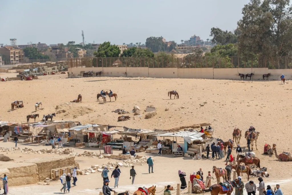 A vibrant desert bazaar with people and camels near the Giza pyramids.