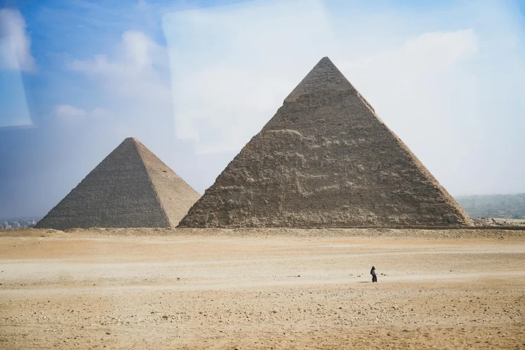 Wide shot of the Pyramids of Giza at daytime with a distant solitary figure.