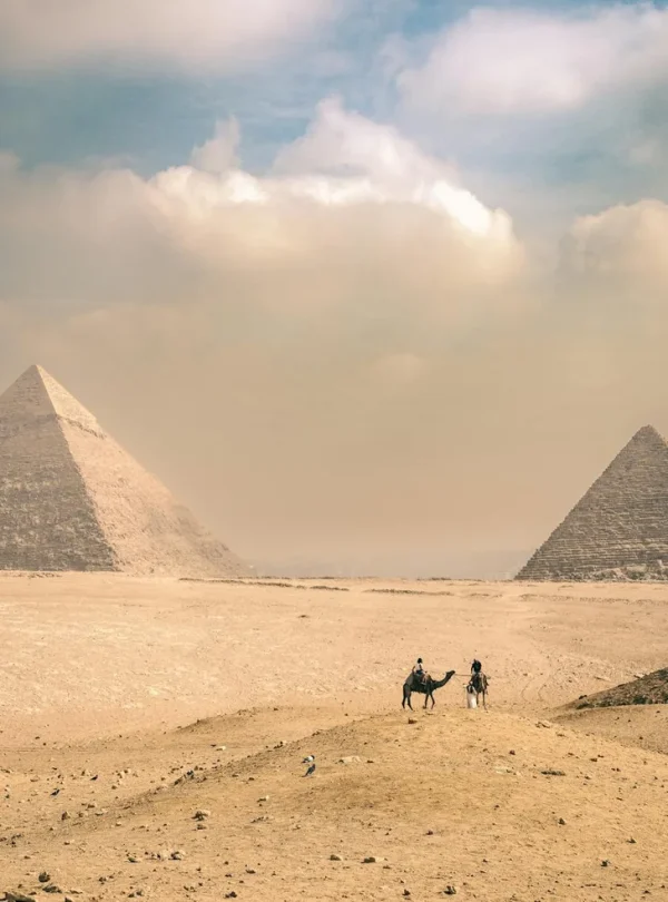 Explore the majestic Pyramids of Giza under a sunny sky with distant travelers on camels.