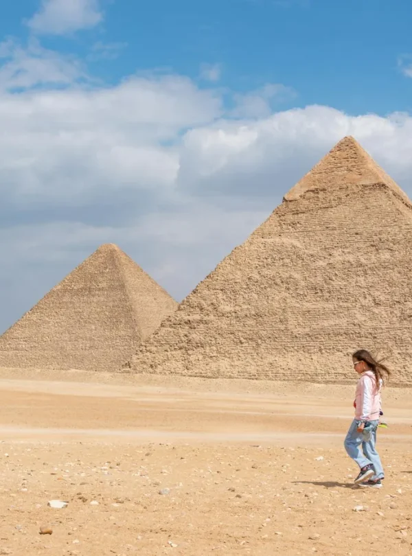 Two women walking near the iconic pyramids of Giza, Egypt, under a bright sky.