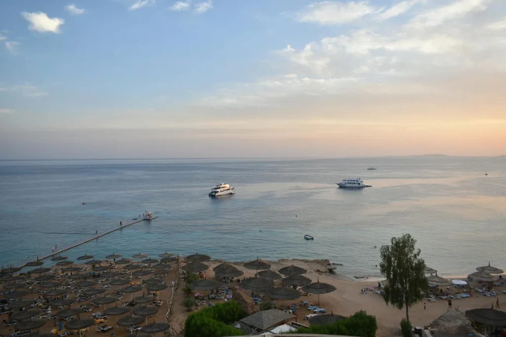 Stunning aerial view of Sharm El Sheikh's beach and sea during sunset with boats and parasols.