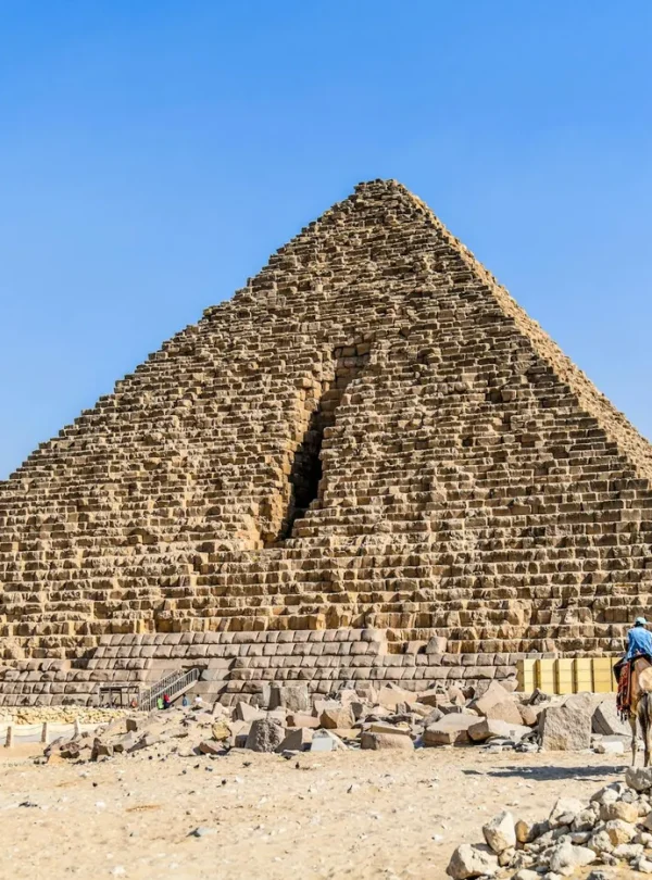 Tourists ride camels near the Pyramid of Khafre in Giza, Egypt, under a clear blue sky.