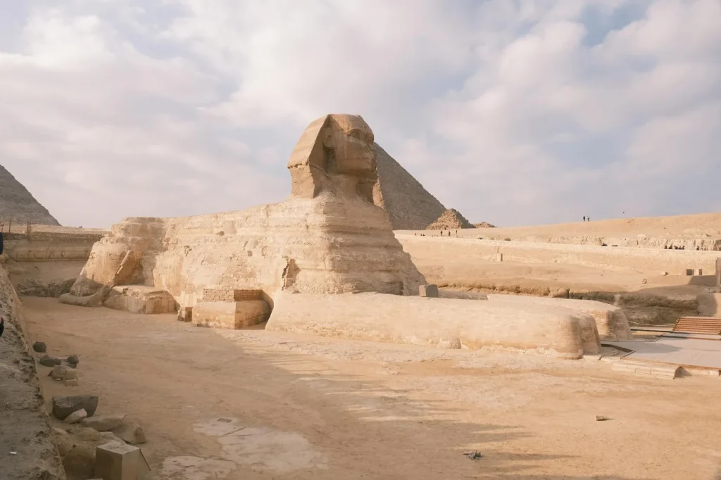 The Great Sphinx of Giza against a backdrop of pyramids and a partly cloudy sky.