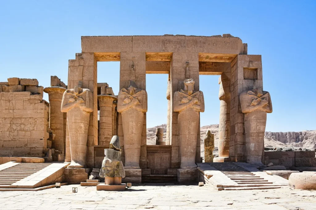 Explore the grand ancient statues and ruins of the Ramesseum in Luxor, Egypt, under a clear blue sky.