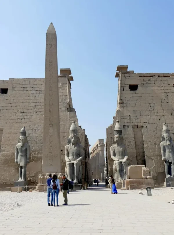 Visitors explore the iconic entrance of Luxor Temple, featuring colossal statues and an obelisk.