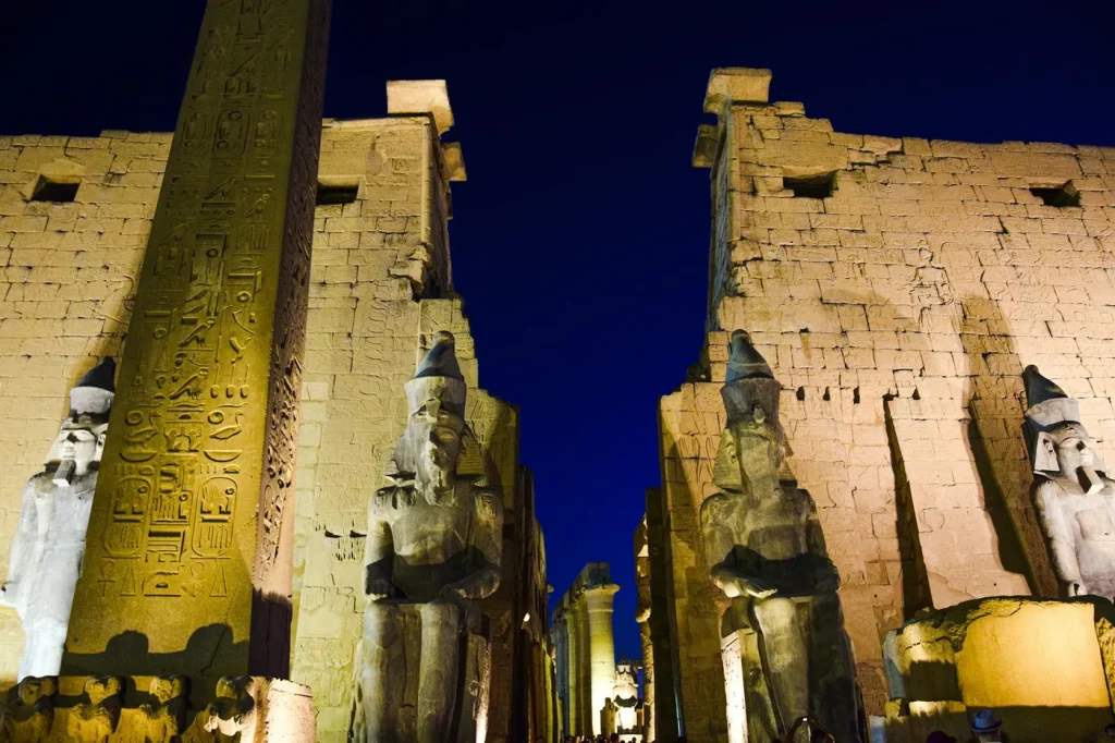 Night view of the illuminated Luxor Temple with ancient statues and hieroglyphs.