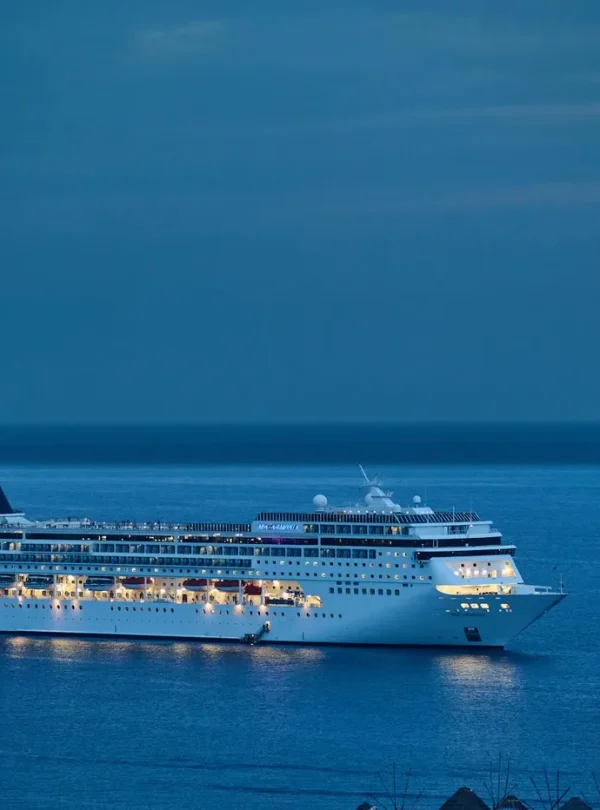 A cruise ship glides through calm waters at dusk, illuminated against the serene evening sky.