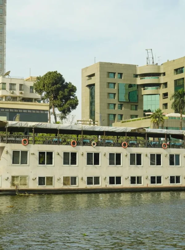 A serene scene of a cruise boat on the Nile River in Cairo, Egypt, with modern buildings in the background.
