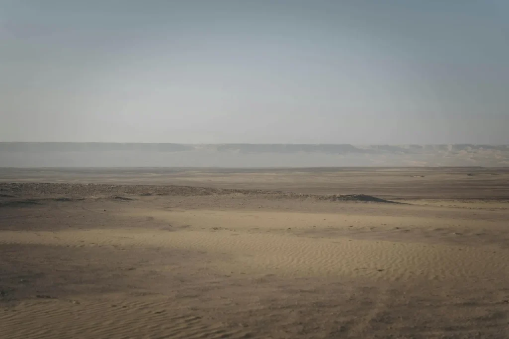 Expansive desert scene at Faiyum Oasis, showcasing sand dunes and arid terrain under a clear sky.